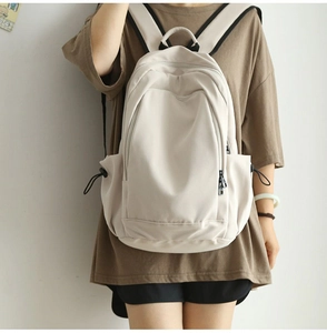 Detail view of cream-white nylon backpack featuring black drawstrings and side pockets