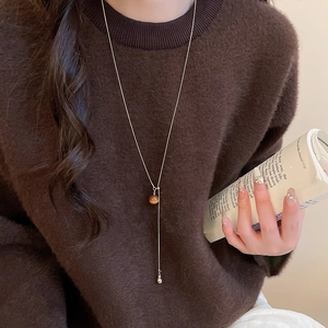 Detail of tiger eye heart pendant on long gold adjustable necklace over brown sweater