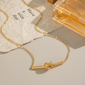 Détail d'un collier avec pendentif noeud doré posé sur un bureau de style minimaliste