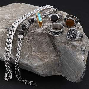 Detail view of men's stainless steel rings and bracelets on a natural rock background