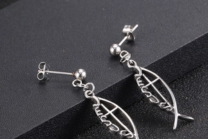 Macro shot of silver titanium fish-shaped earrings with Jesus engraving on black background