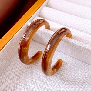 Detailed view of amber resin C-shaped earrings with tortoise shell pattern on beige fabric