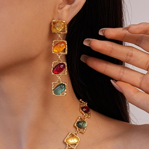 Close-up of geometric gold earrings with colorful square resin stones on model