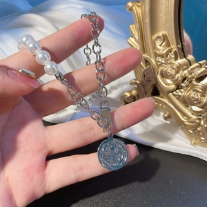 Close-up of pearl and silver chain bracelet with a relief pendant on white silk background