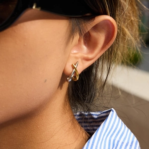 Close-up of model wearing two-tone gold and silver crisscross stainless steel earrings