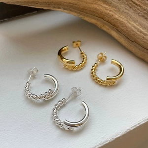 Detail of twisted C-shape earrings in gold and silver finish with minimalist aesthetics