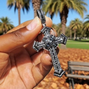 Hip hop cross pendant necklace with black stones held by hand in a sunny outdoor setting