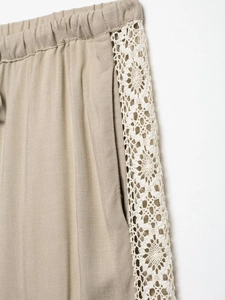 Detailed close-up of beige linen wide-leg pants featuring white hollow lace side trim