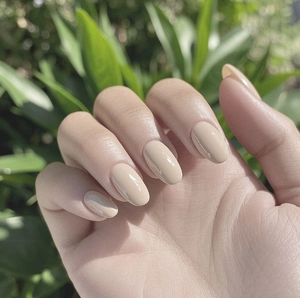 Primer plano de uñas postizas nude brillantes en forma de almendra en la mano sobre fondo natural