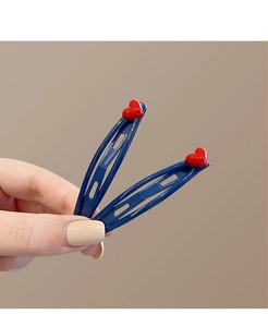 Close-up of navy blue metal BB hair clips with 3D bright red heart charms on a warm background