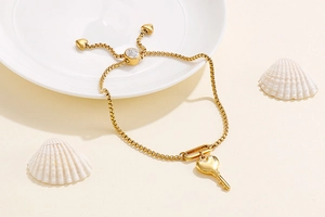 Gros plan du bracelet doré à clé en forme de cœur avec fermoir réglable sur fond beige
