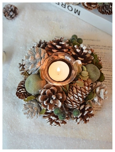 Detail of pine cones, red berries and snow decor on a clear glass candle holder