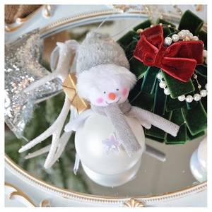 Close-up of plush snowman doll and green velvet tree ornament with red bow and pearls