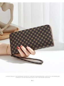 Detail of dark brown leather long wallet with gold clover pattern and hand strap