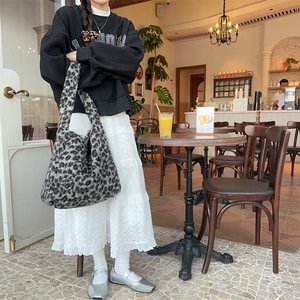 Detail shot of a large faux fur leopard print tote bag styled in a cozy indoor cafe setting