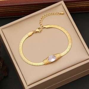 Detail of gold snake chain bracelet with oval clear gemstone in a beige jewelry box