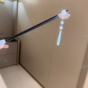 Detailed shot of fan-shaped silver ornament and light green tassel on a wooden hair stick