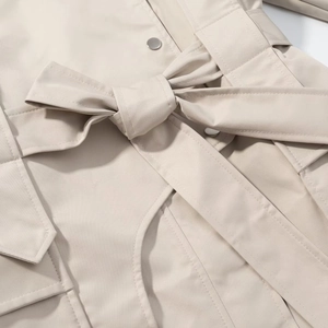 Detail of waist tie belt with a large bow on beige trench coat with metallic snap buttons