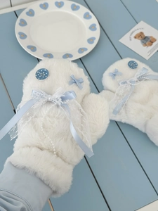 Detail of plush mittens with blue bow, white lace, and pearl beads on soft faux fur