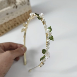 Detail of elegant gold headband with white enamel flowers, pearls and green leaves