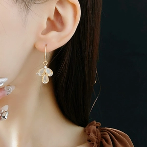 Close-up of teardrop opal earrings with rhinestones shown on a model on black background