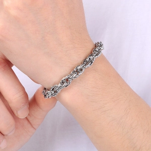 Bracelet chaîne torsadée en acier inoxydable argenté porté au poignet sur tissu blanc