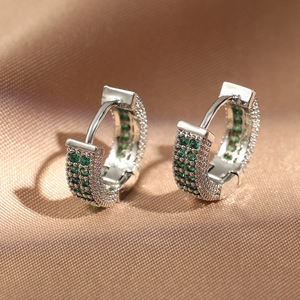 Elegant silver hoop earrings with pave-set green crystals on luxurious silk background