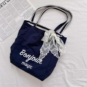 Detail of navy canvas tote with white Bonjour lettering and striped handles on newspaper