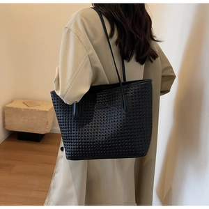 Detail of the black woven texture tote bag with slim shoulder straps on a beige trench coat