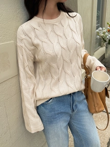 Detail of beige cable-knit sweater texture styled with jeans and a leather bag