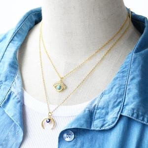 Detail of double-layer golden evil eye necklace with rhinestones and crescent moon charm