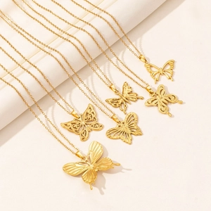 Detail showing five different gold-colored butterfly pendant necklaces on beige fabric