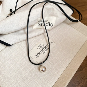 Close-up of minimalist silver spherical pendant on black cord over a textile background