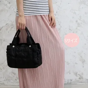 Model holding a small black quilted nylon tote bag in S size with silver rivets