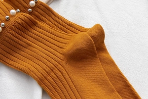 Detail of mustard yellow ribbed socks featuring elegant pearl and metal stud embellishments