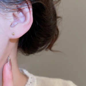 Macro shot of minimalist small gold ball stud earrings worn for a sleek everyday jewelry look