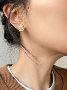 Detail of gold-plated gourd stud earrings with yellow cubic zirconia on model