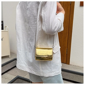 Detail of a golden crocodile embossed mini chain bag worn as a crossbody accessory