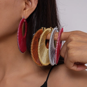 Close-up of woven geometric hoop earrings in vibrant metallic red, orange, gold and silver