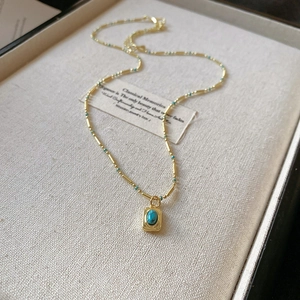 Macro detail of golden chain necklace with turquoise pendant on elegant beige background