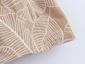Detail of white leaf embroidery on light coffee flat weave fabric showing texture