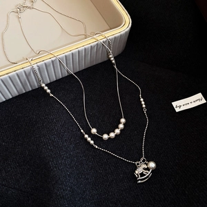 Close-up of double-layer silver necklace featuring pearl beads and a zircon rocking horse charm