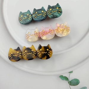 Three cute acetate cat hair clips in green, pink, and tortoiseshell on a white plate