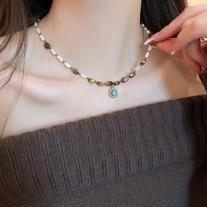 Detail of beaded necklace featuring tiger eye stones and turquoise teardrop pendant