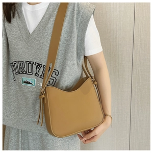 Détail du sac à bandoulière demi-lune en cuir mat marron porté par un mannequin chic