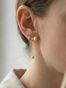 Close-up of elegant gold bow tassel earring worn by model showing exquisite metal detail
