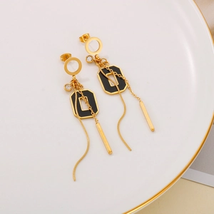 Détail de boucles d'oreilles dorées à pampilles avec accents noirs et un strass brillant
