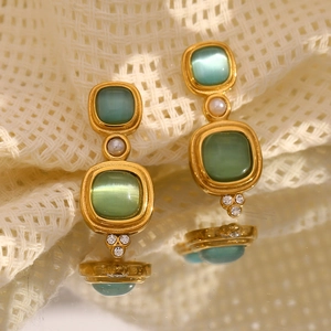 Macro de boucles d'oreilles dorées 18K avec œil de chat vert et perles sur tissu blanc