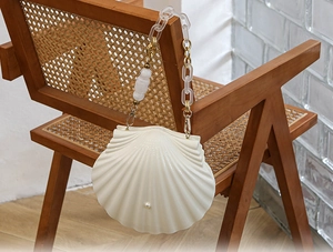 Detail of a shell-shaped cream bag with acrylic chain hanging on a wooden chair