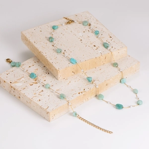 Golden necklace with light green gravel stones and small white pearls on a travertine stand